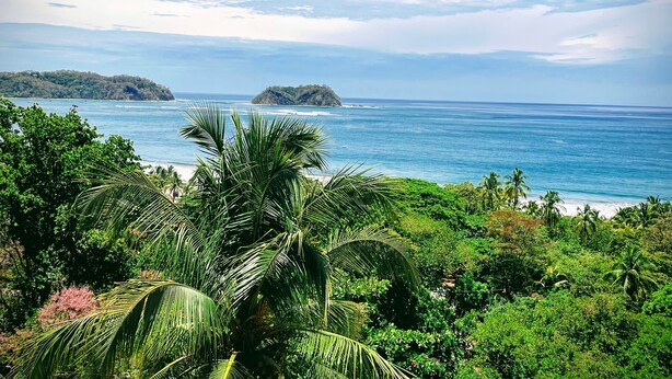 A tropical beach with dense greenery, a clear blue sea, and distant islands. - Casa Pura Vida (Sámara)