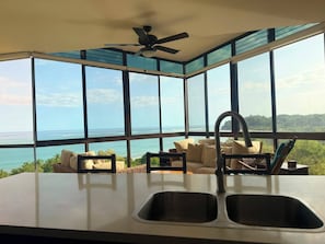 Eine moderne Küche mit großen Fenstern, einem Deckenventilator und Meerblick.