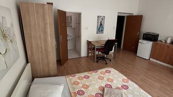 A bedroom with a bed, a desk, a chair, and a kitchenette.