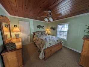 A bedroom with a wooden ceiling, a bed with floral bedding, a ceiling fan, a window with blinds, and a dresser. - Cute Beachy Bungalow-walking distance to beach-3 bd/2 ba house in NMB (North Myrtle Beach)