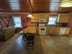 A kitchen with wooden cabinets, a granite countertop, a white stove, and a dining area with a table and chairs. - Cute Beachy Bungalow-walking distance to beach-3 bd/2 ba house in NMB (North Myrtle Beach)