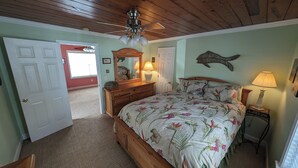 Un dormitorio con techo de madera, una cama con ropa de cama floral, un aparador, un espejo y una decoración de peces colgada en la pared.