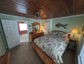 A bedroom with a wooden ceiling, a bed with floral bedding, a dresser, a mirror, and a wall-mounted fish decoration. - Cute Beachy Bungalow-walking distance to beach-3 bd/2 ba house in NMB (North Myrtle Beach)