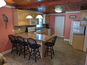 A kitchen with wooden cabinets, a granite countertop, a microwave, and a refrigerator. - Cute Beachy Bungalow-walking distance to beach-3 bd/2 ba house in NMB (North Myrtle Beach)
