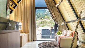 Ein modernes Interieur mit Balkon, einer Sitzecke und Blick auf eine hügelige Landschaft.