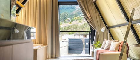 A modern interior with a balcony, a sofa, and a view of a hilly landscape.