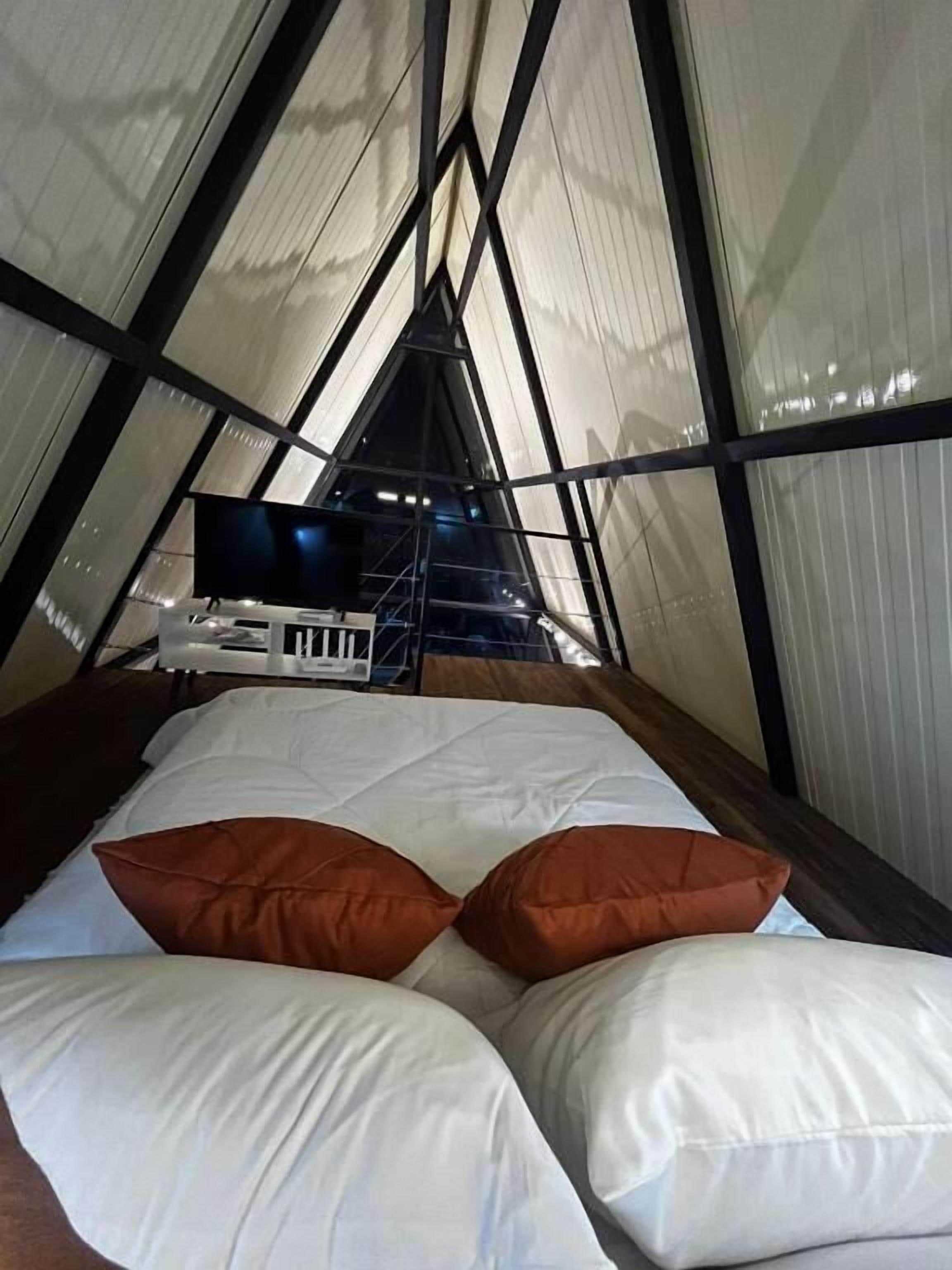 A triangular room with a bed, pillows, and a television.