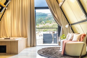 A room with a sofa, a small table, and a view of a hillside.