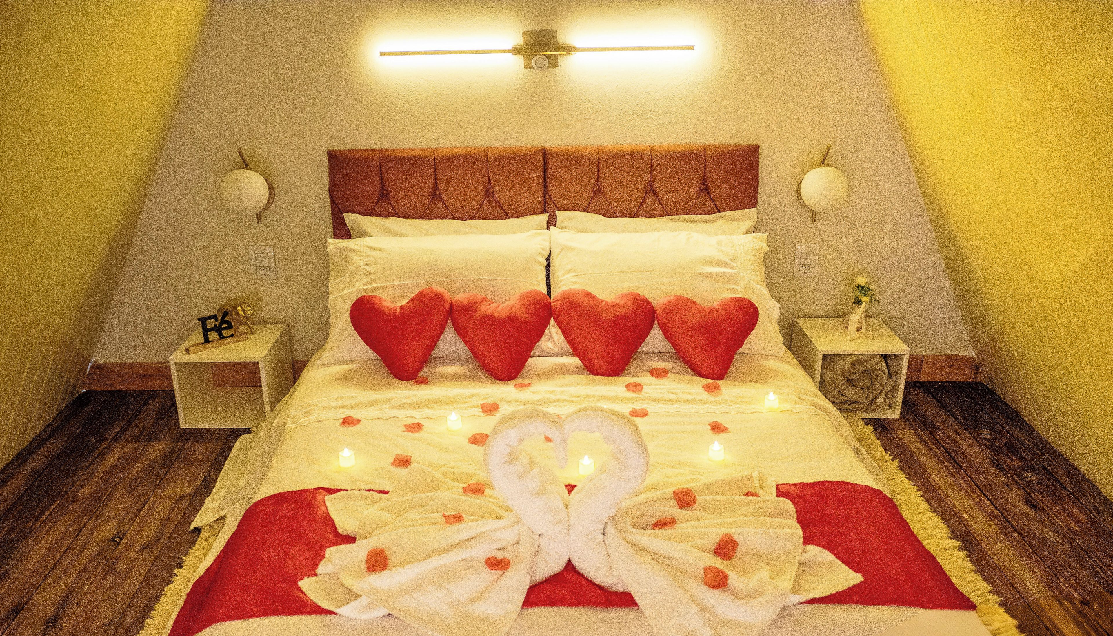 A bed with heart-shaped pillows, a white towel arrangement, and a lit candle.