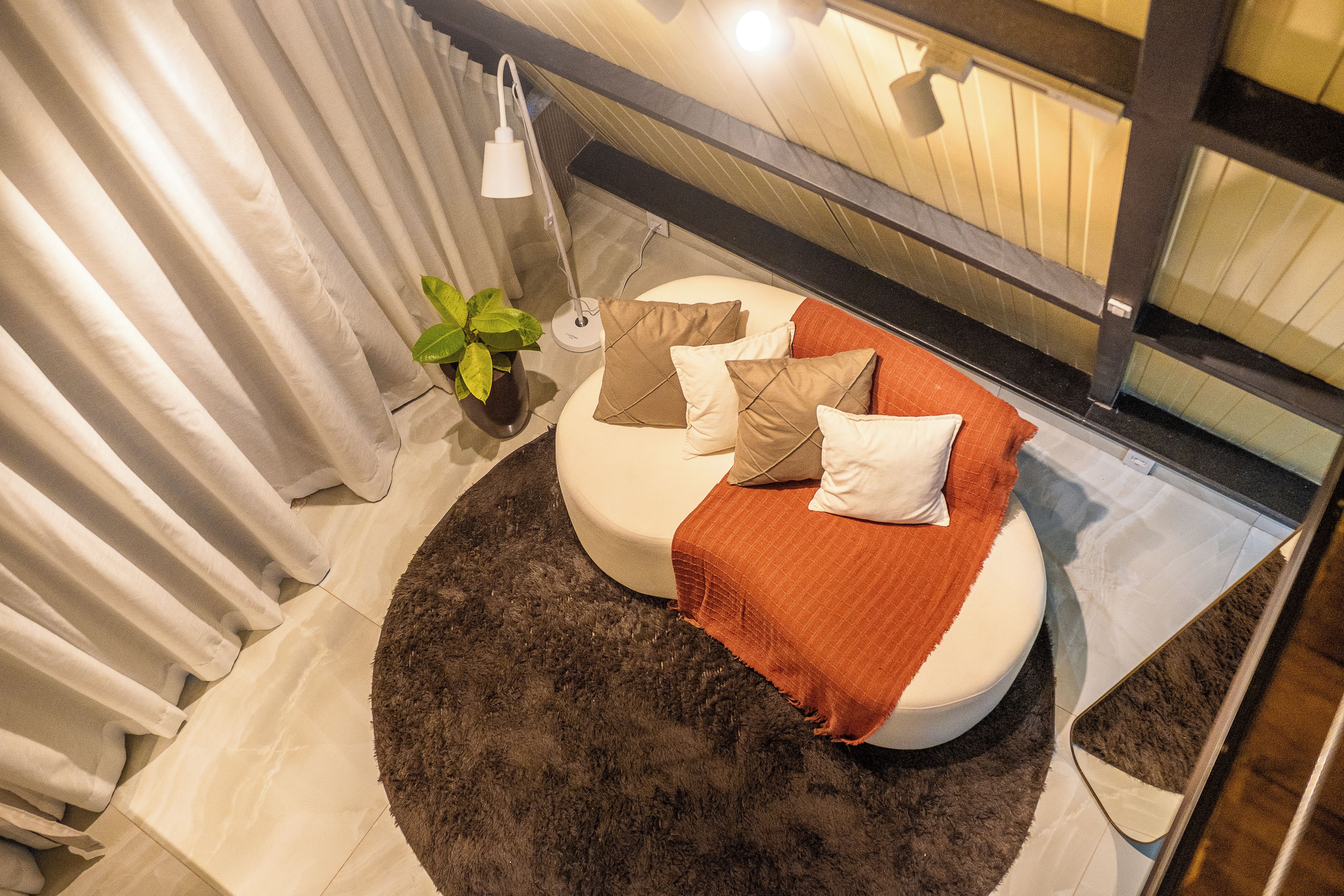 Un lit rond, surmonté d’un tapis foncé, avec une plante en pot et une lampe de chevet.