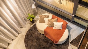 Un lit rond, surmonté d’un tapis foncé, avec une plante en pot et une lampe de chevet.
