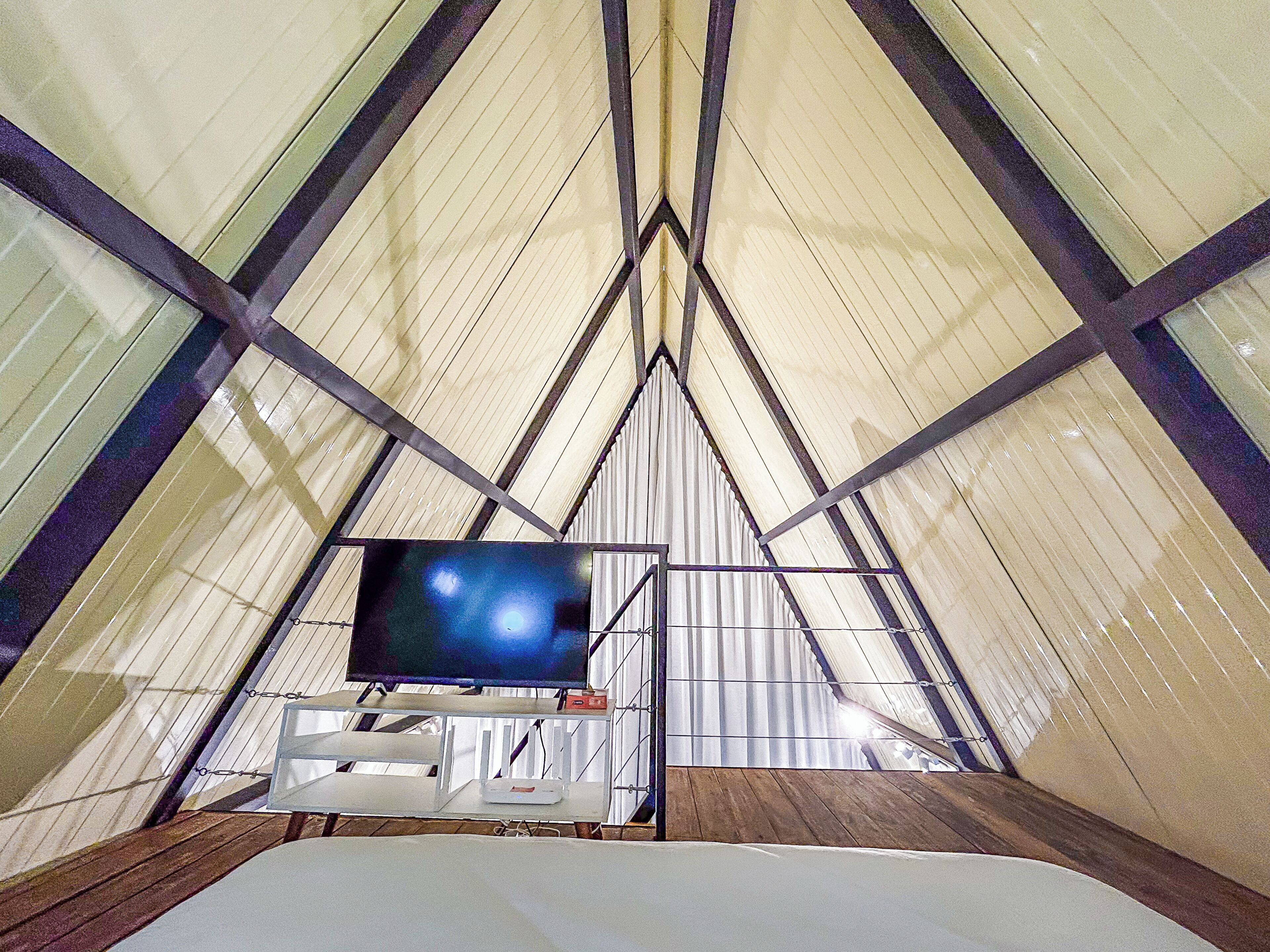 A tent-like structure with a television mounted on a stand, a white table, and a wooden floor.