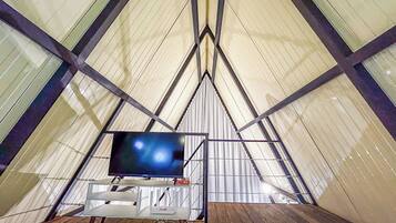 A tent-like structure with a television mounted on a stand, a white table, and a wooden floor.
