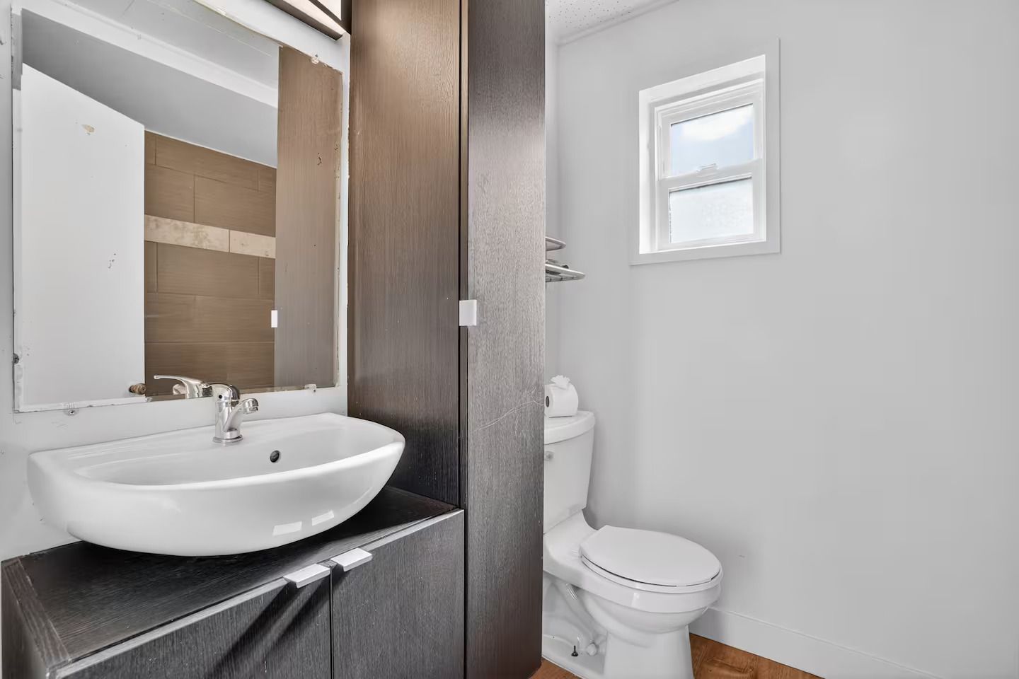 A bathroom with a white sink, a mirror, a toilet, and a window.