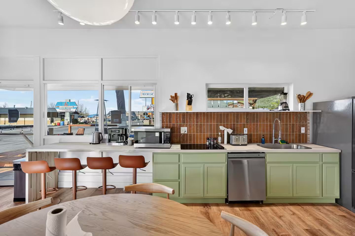 A modern kitchen with a large island, green cabinets, and a view of a restaurant through the window.
