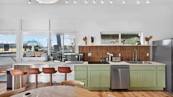 A modern kitchen with a large island, green cabinets, and a view of a restaurant through the window.