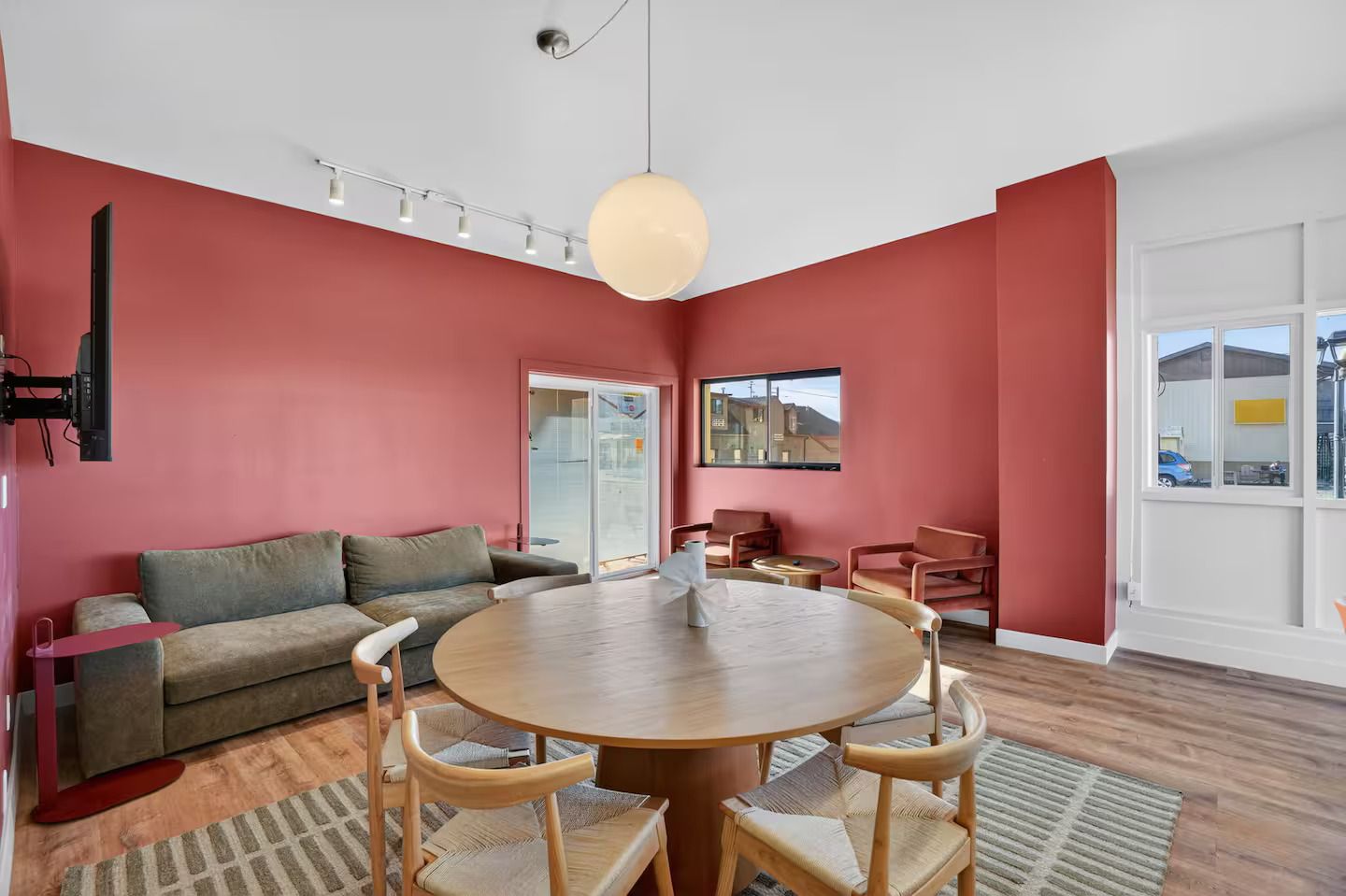A modern living room with a round wooden table, red walls, and a large window.