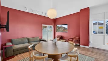 A modern living room with a round wooden table, red walls, and a large window.
