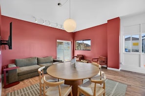 Una sala de estar moderna con una mesa redonda de madera, paredes rojas y un ventanal grande.