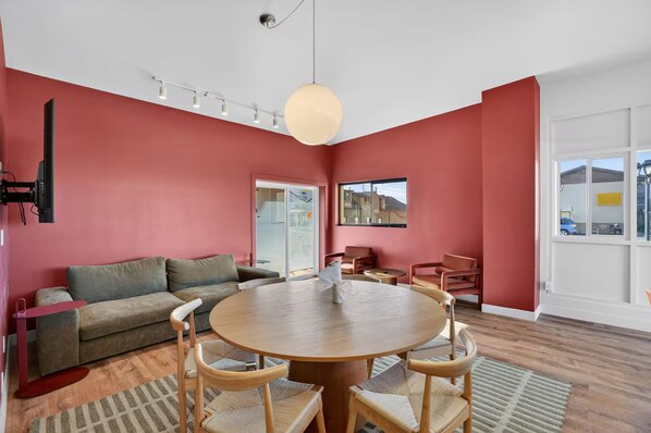 A modern living room with a round wooden table, red walls, and a large window. - Highlander Motel (Williams)