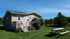 A single-story house with a porch, a picnic table, and a well-maintained lawn.