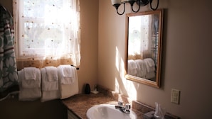 A bathroom with a sink, mirror, window with curtains, and towels.