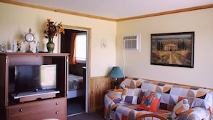 A room with a TV, a sofa, a painting, and a lamp.