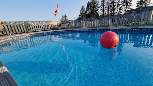 A swimming pool with a red ball, clear blue water, and a flag.