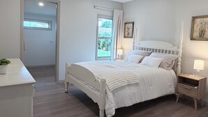 Une chambre à coucher avec un lit à baldaquin blanc, une table de chevet avec une lampe et une fenêtre avec des rideaux.