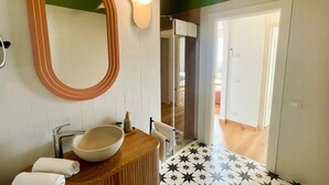A bathroom with a large oval mirror, a wooden vanity, a bowl sink, a shower, and a patterned floor. - 2-bedroom apartment in tranquil Brenzone sul Garda with AC (Brenzone sul Garda)