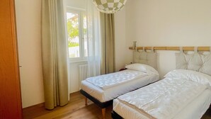 A bedroom with two beds, a checkered hanging light, a window with curtains, and a radiator. - 2-bedroom apartment in tranquil Brenzone sul Garda with AC (Brenzone sul Garda)