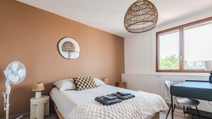 A bedroom with a bed, a desk, a chair, a standing fan, a lamp, and a window. - Le Grandval - Spacious 3 rooms (Reims)