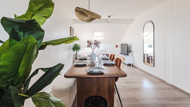 A dining area with a wooden table set for four, a hanging light fixture, and a large mirror on the wall. - Le Grandval - Spacious 3 rooms (Reims)