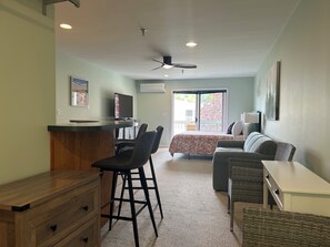 A room with a bed, a desk, chairs, a television, and a ceiling fan. - Welcome to Wellington Manor Condo, a cozy studio vacation rental in Wells, Maine, perfectly located near Wells Beach, local restaurants, shopping, and popular Southern Maine coastal attractions. This comfortable Wells studio condo is ideal for couple (Wells)