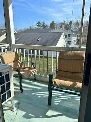 A porch with two chairs and a table, overlooking a residential area with houses and trees.