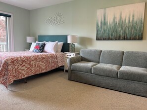 A bedroom with a bed, a grey sofa, a nightstand, a lamp, and a wall art piece.