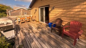 Een houten terras met tuinmeubilair, een barbecue en een overdekt gedeelte met een deur.