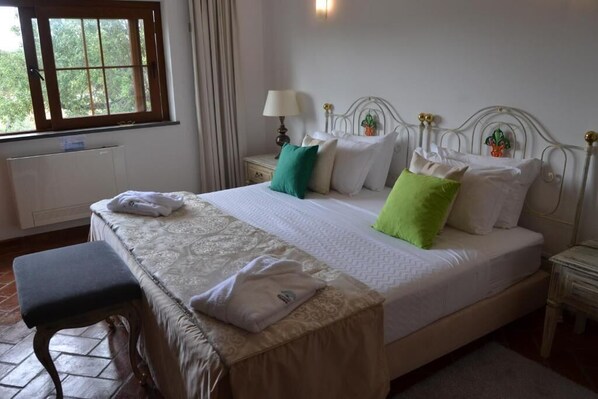 A neatly made bed with a patterned bedspread, a bedside table with a lamp, and a window with curtains.