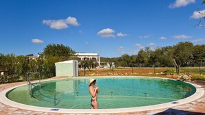 Una piscina con una persona en traje de baño, rodeada de pavimento y árboles.