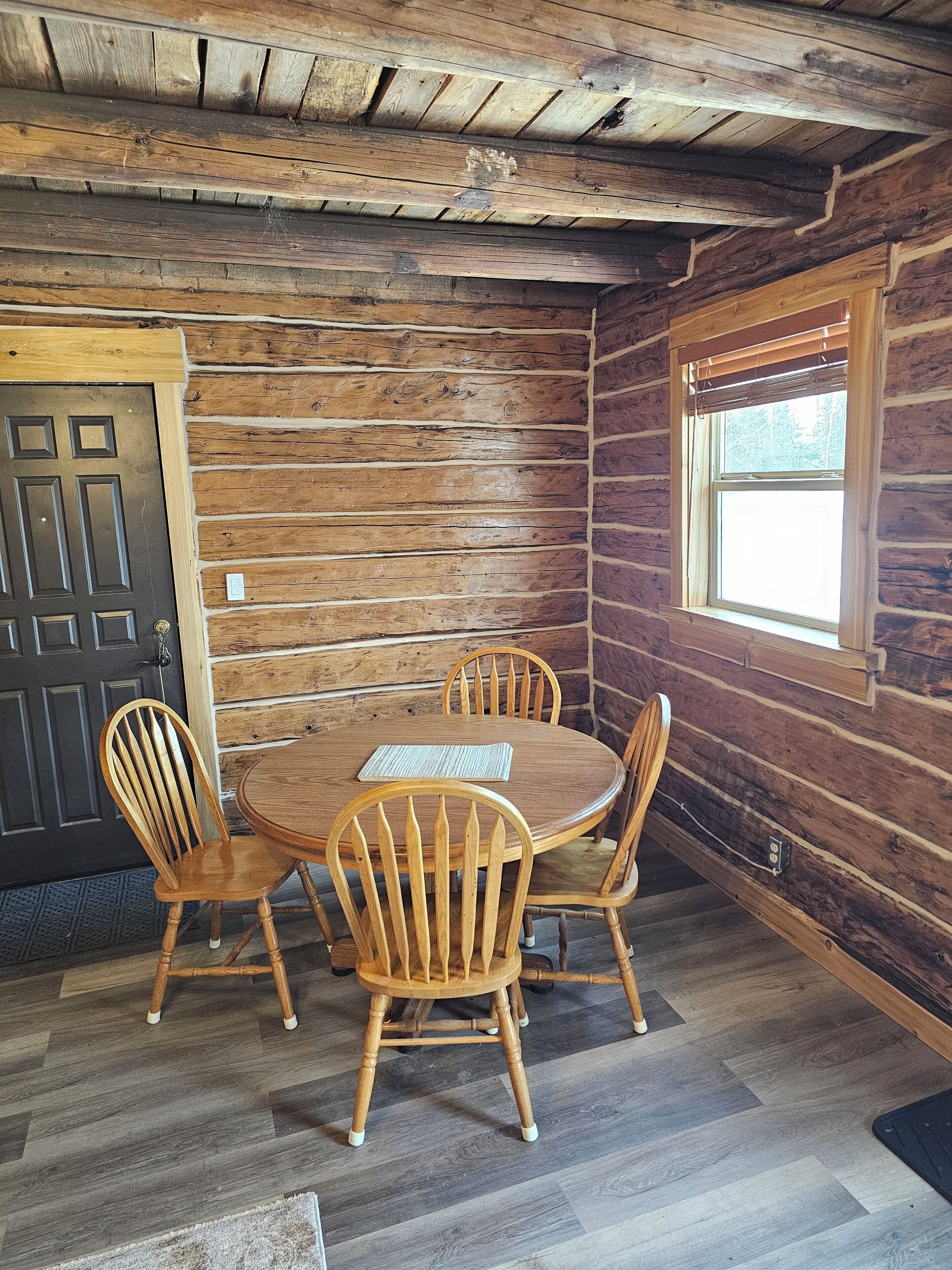 A wooden interior with a round table and four chairs, a door, and a window.