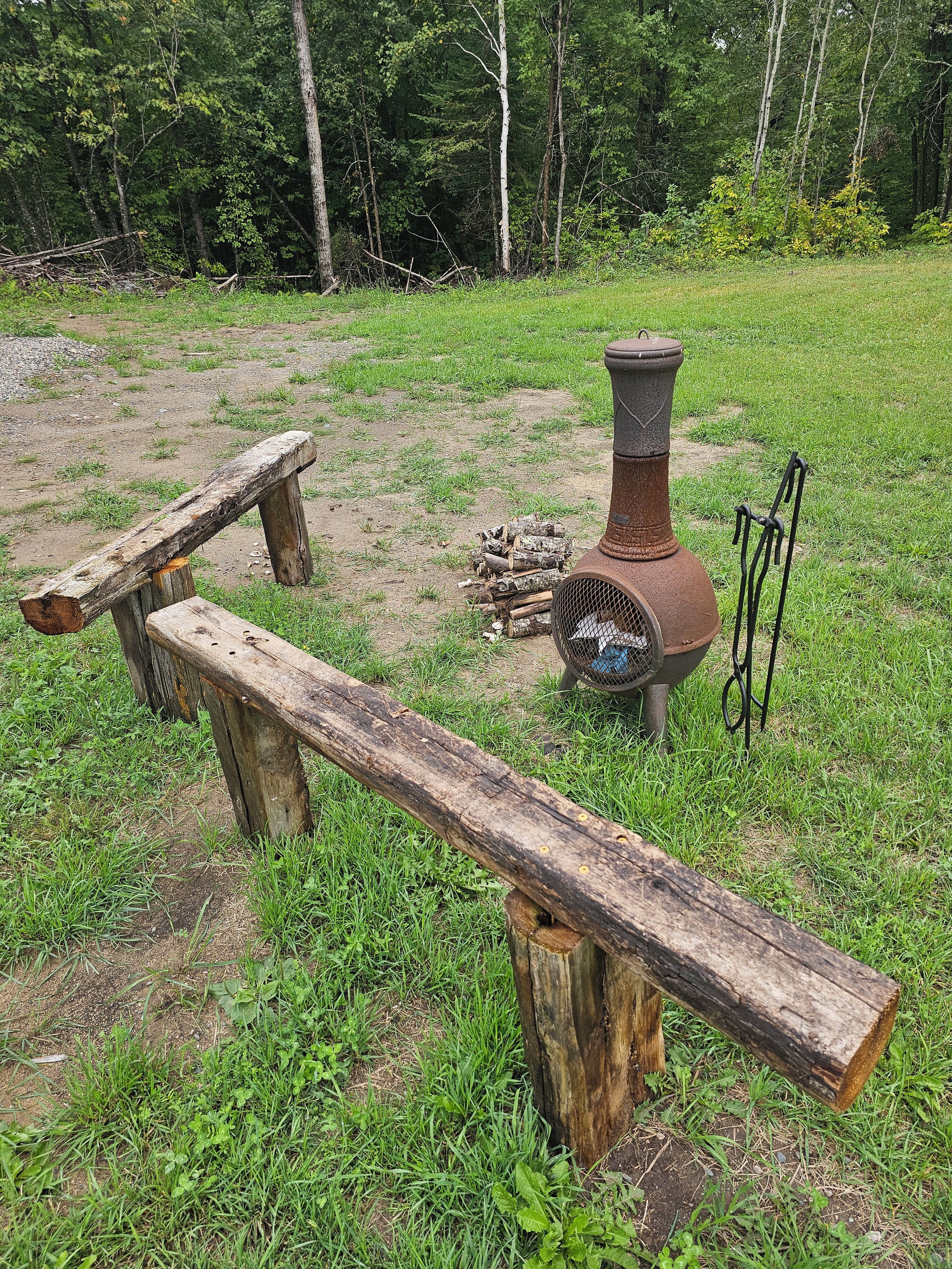 Un entorno rústico al aire libre con un banco de madera, una parrilla metálica y un brasero.