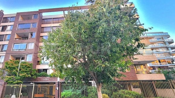 Ein mehrstöckiges Wohngebäude mit Balkonen, einem verschlossenen Eingang und einem Baum im Vordergrund.