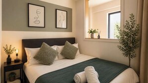 A neatly made bed with a green bedspread, two pillows, and rolled towels on a nightstand with a small plant. - 2 BEDROOM 2.5 BATHROOM - MODERN - OLD TRAFFORD - CITY CENTRE (Manchester)