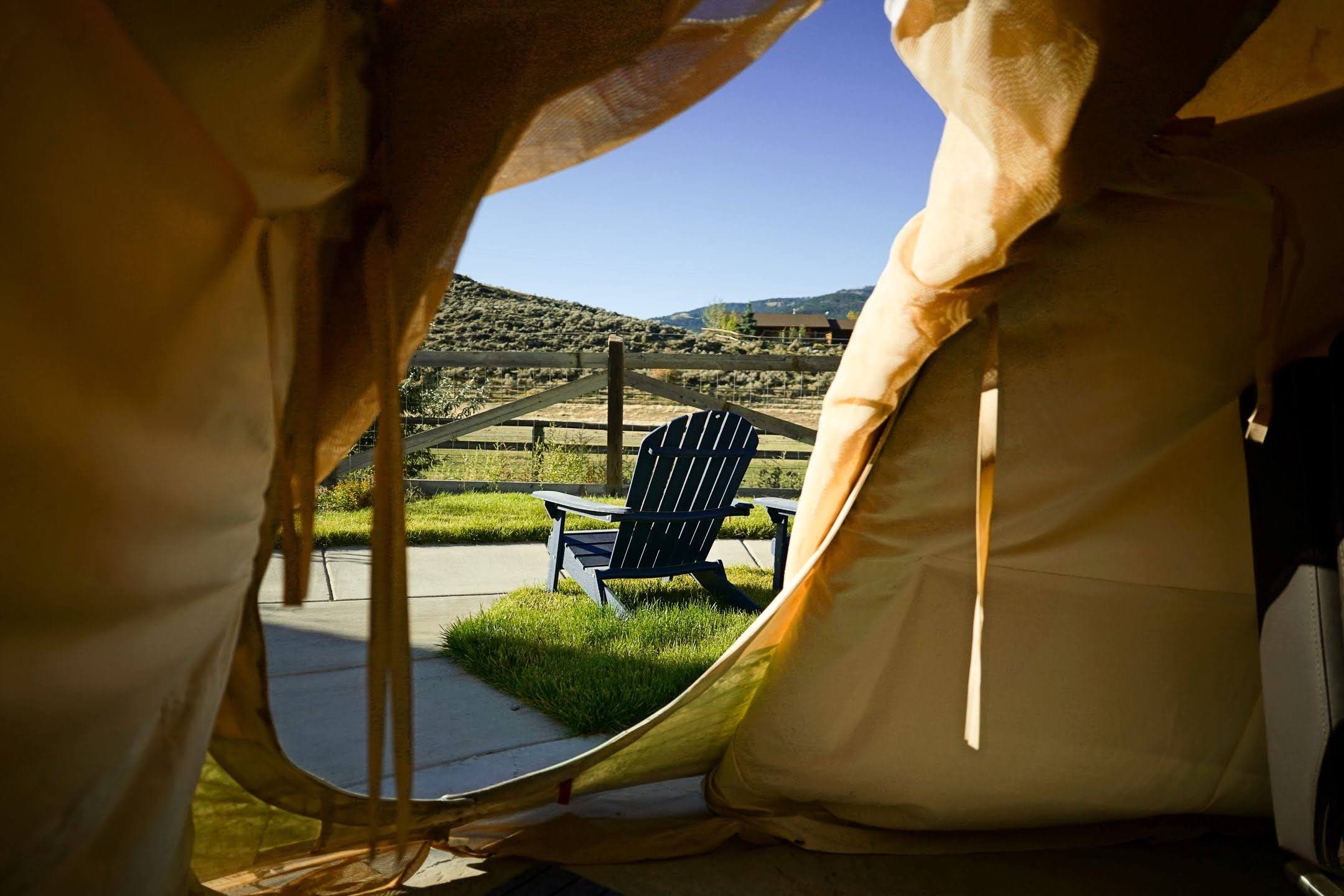 Een tent met uitzicht op een grasveld en een zwarte stoel erbuiten.