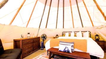 A tent with a bed, a dresser, a bench, and a fan.