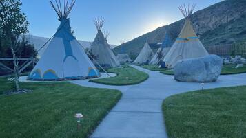 Un sendero conduce a varias tiendas tipi, con un área de césped y una montaña al fondo.