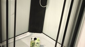 A corner shower with a handheld showerhead, a white floor, and two bottles of shampoo and conditioner. - Stay in Dunkirk: Room Near Malo Beach and Shops (Dunkerque)