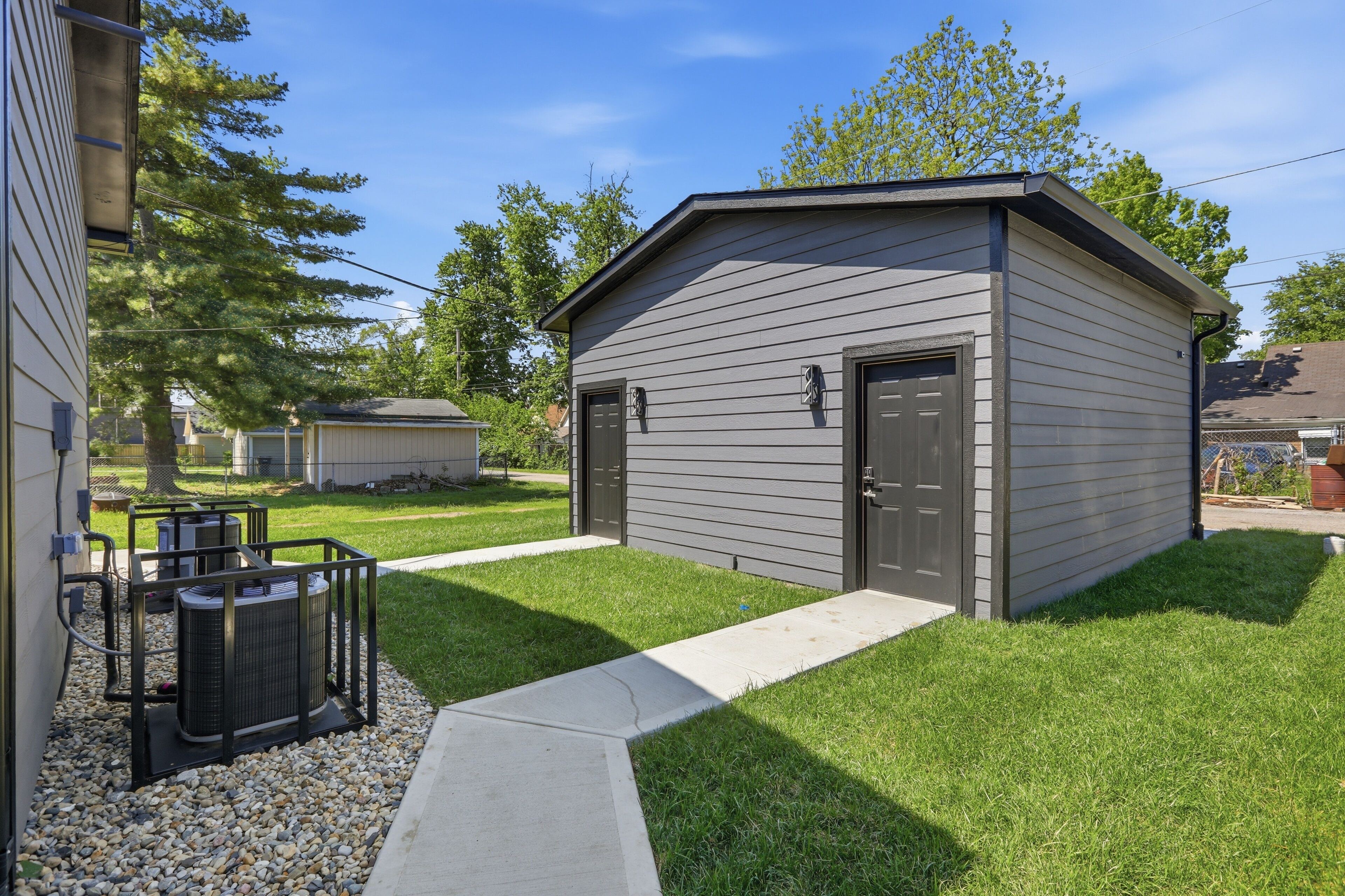 A small, single-story building with a dark exterior, a front door, and a small porch area with a concrete path leading to it.
