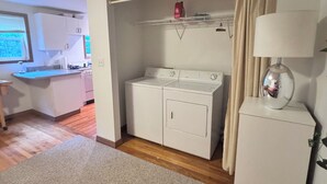 A compact room with a washing machine, a small cabinet, a lamp, and a window.