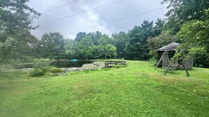 A grassy area with a pond, a wooden swing set, and a gazebo.